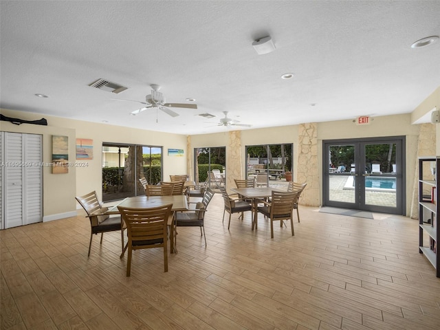 dining space featuring french doors, light wood-type flooring, a textured ceiling, and ceiling fan