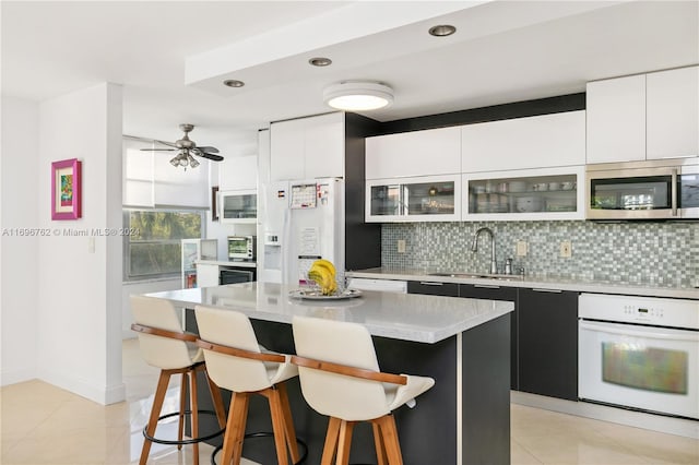 kitchen with white cabinetry, a center island, ceiling fan, and white appliances