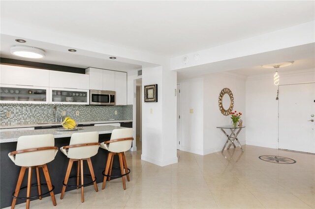 kitchen with backsplash, a breakfast bar, sink, light tile patterned floors, and white cabinets