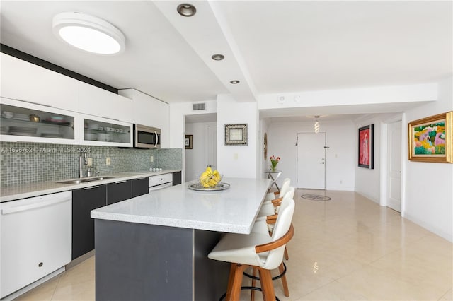 kitchen featuring backsplash, white cabinets, sink, dishwasher, and a center island