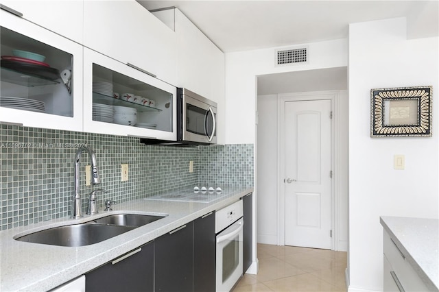 kitchen featuring tasteful backsplash, white oven, sink, light tile patterned floors, and white cabinets