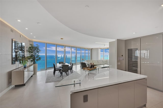 kitchen featuring light stone countertops, a center island, hanging light fixtures, expansive windows, and a water view