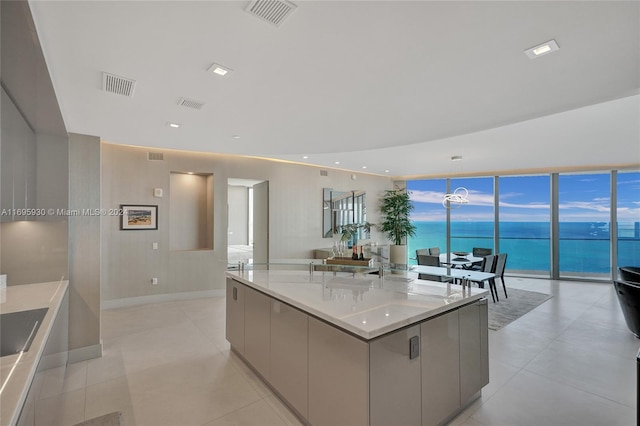 kitchen featuring light stone counters, a wealth of natural light, gray cabinetry, a spacious island, and a water view