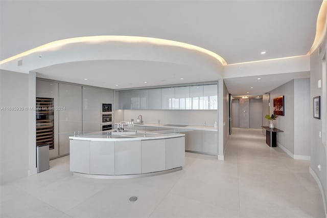 kitchen featuring light tile patterned floors, wine cooler, oven, a kitchen island with sink, and white cabinets