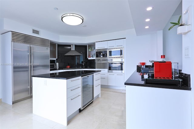 kitchen with white cabinets, built in appliances, wine cooler, and wall chimney exhaust hood