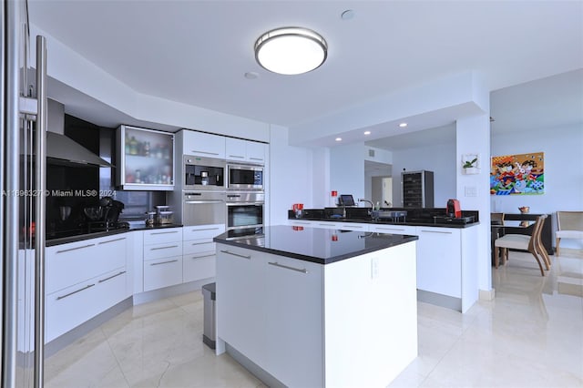 kitchen featuring white cabinets, wall chimney exhaust hood, a kitchen island, and decorative backsplash