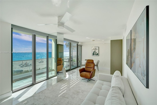 living room featuring a water view, a wall of windows, ceiling fan, and a view of the beach