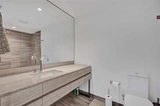 bathroom with toilet, a tile shower, and vanity