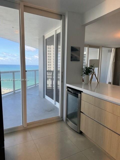 kitchen featuring stainless steel dishwasher, light brown cabinets, a water view, a beach view, and light tile patterned flooring