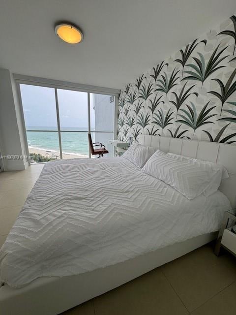 bedroom with a water view, light tile patterned floors, and a view of the beach