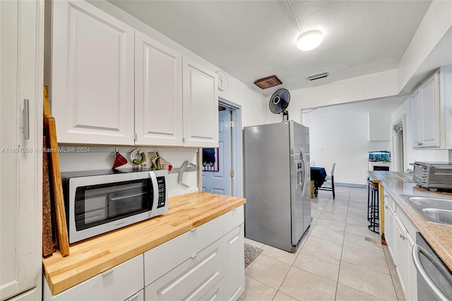 kitchen featuring white cabinets, light tile patterned floors, stainless steel appliances, and wooden counters