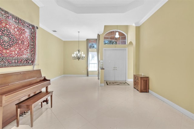 foyer entrance featuring a raised ceiling, light tile patterned flooring, ornamental molding, and a notable chandelier