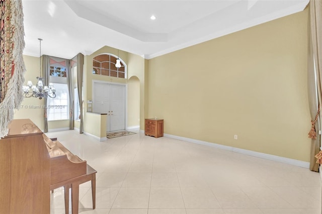 tiled foyer entrance with a raised ceiling, crown molding, and a notable chandelier