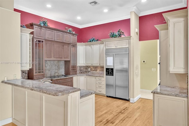 kitchen with kitchen peninsula, light stone counters, stainless steel built in refrigerator, crown molding, and light hardwood / wood-style flooring