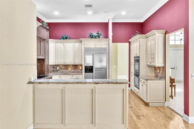 kitchen with built in refrigerator, light stone countertops, ornamental molding, light hardwood / wood-style floors, and kitchen peninsula