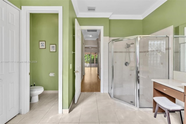 bathroom featuring tile patterned flooring, toilet, ornamental molding, and a shower with door