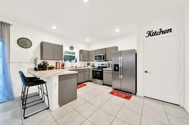 kitchen featuring a kitchen breakfast bar, gray cabinets, light tile patterned flooring, kitchen peninsula, and stainless steel appliances