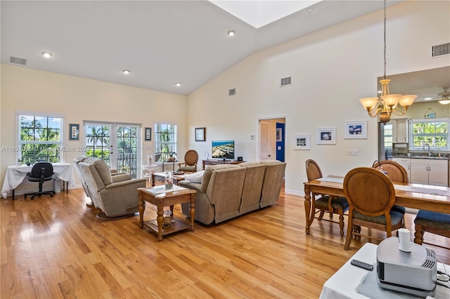 living room featuring ceiling fan with notable chandelier, light wood-type flooring, sink, and high vaulted ceiling