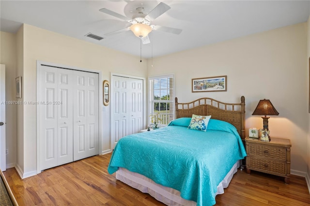 bedroom with hardwood / wood-style flooring, ceiling fan, and multiple closets