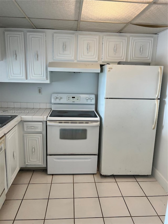 kitchen with a drop ceiling, white appliances, exhaust hood, white cabinets, and light tile patterned flooring