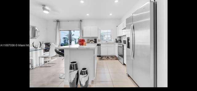 kitchen with appliances with stainless steel finishes, light stone counters, a kitchen island, white cabinetry, and light tile patterned flooring