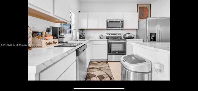 kitchen with light stone countertops, sink, white cabinetry, and stainless steel appliances