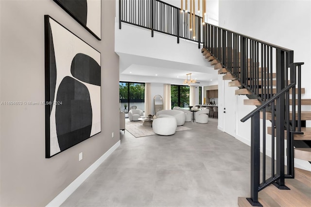 stairway featuring a notable chandelier, a high ceiling, and concrete floors