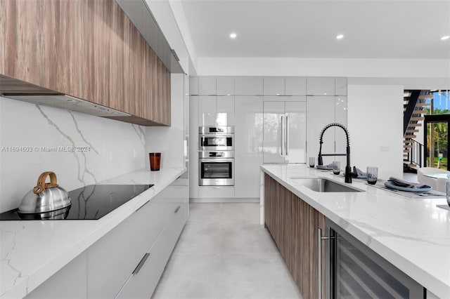 kitchen featuring white cabinets, sink, black electric cooktop, double oven, and beverage cooler