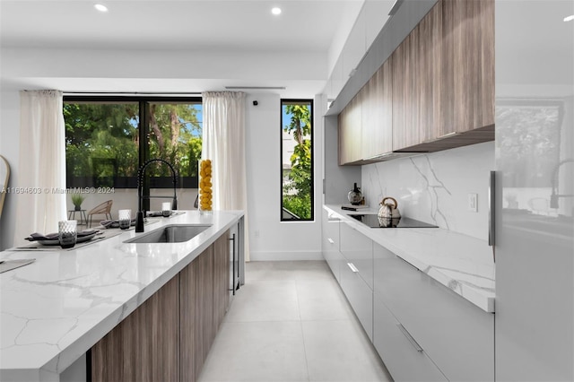 kitchen with backsplash, black electric stovetop, sink, light stone countertops, and light tile patterned floors