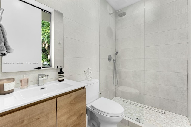 bathroom with decorative backsplash, vanity, tiled shower, tile walls, and toilet