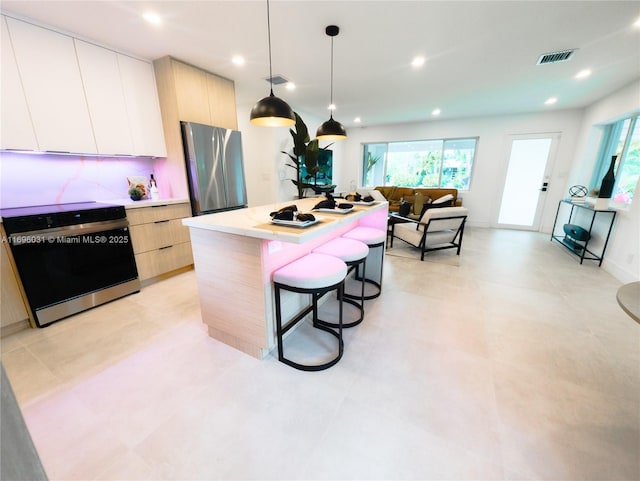 kitchen with appliances with stainless steel finishes, light brown cabinetry, white cabinets, hanging light fixtures, and a kitchen island with sink