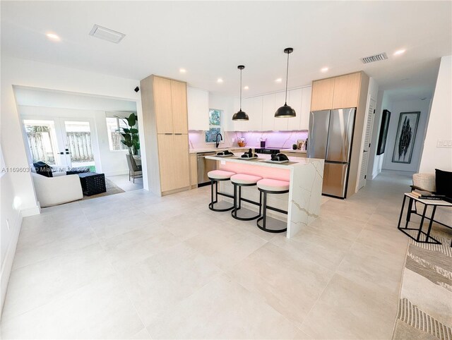 kitchen with stainless steel appliances, pendant lighting, light brown cabinets, white cabinets, and an island with sink