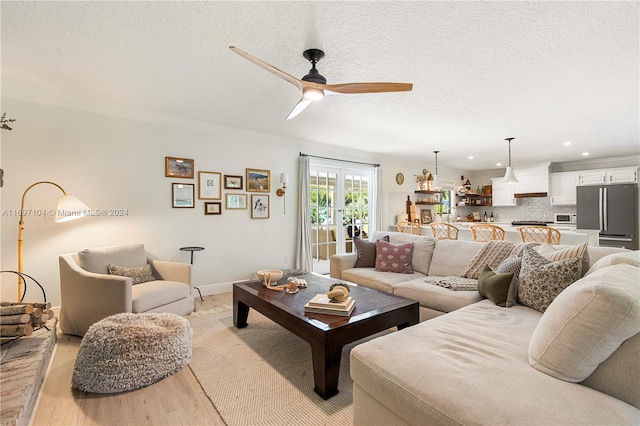 living room featuring ceiling fan, light hardwood / wood-style floors, ornamental molding, and a textured ceiling