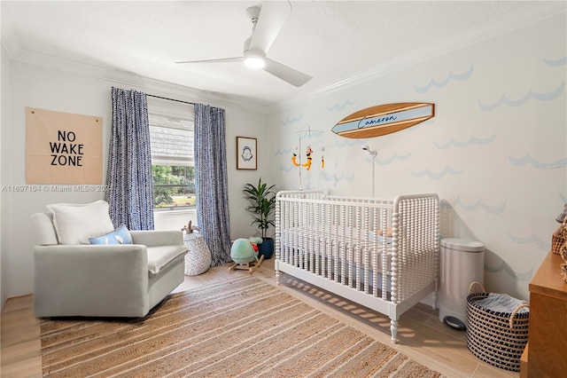 bedroom featuring hardwood / wood-style floors, a nursery area, ornamental molding, and ceiling fan