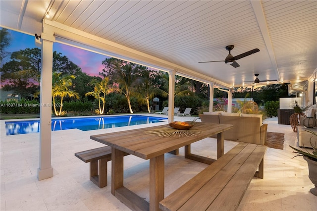 pool at dusk featuring ceiling fan and a patio