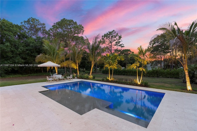 pool at dusk with a yard and a patio