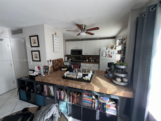 kitchen featuring tile countertops, white refrigerator, electric range, light tile patterned floors, and white cabinetry