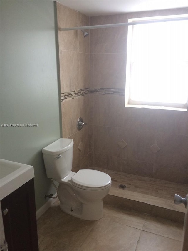 bathroom featuring tile patterned flooring, a tile shower, vanity, and toilet