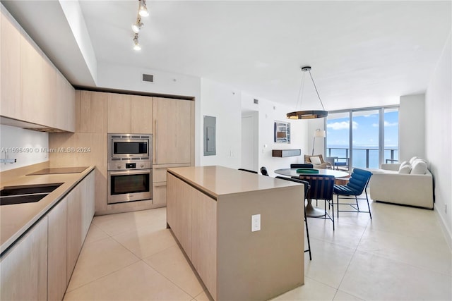 kitchen featuring appliances with stainless steel finishes, light brown cabinets, a water view, a center island, and hanging light fixtures