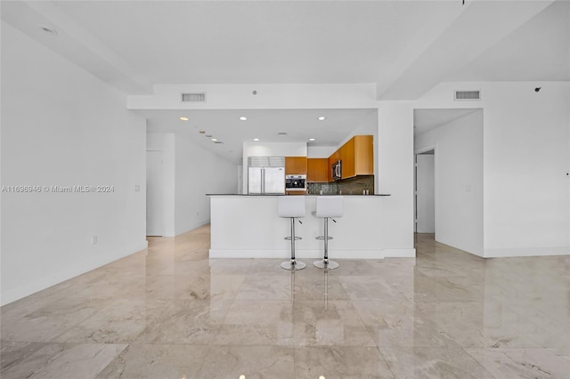 kitchen featuring a kitchen breakfast bar, kitchen peninsula, built in refrigerator, and backsplash