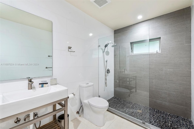 bathroom with tile patterned floors, a tile shower, toilet, and tile walls