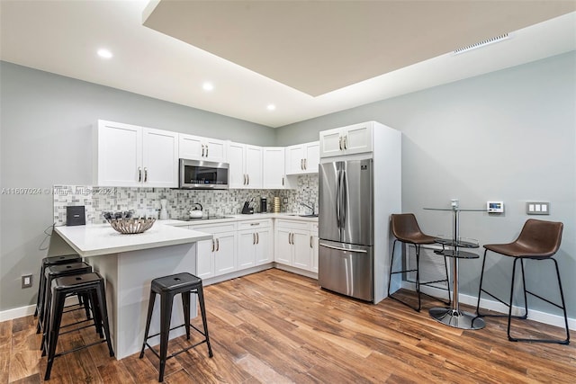 kitchen with hardwood / wood-style floors, white cabinets, a breakfast bar area, kitchen peninsula, and stainless steel appliances