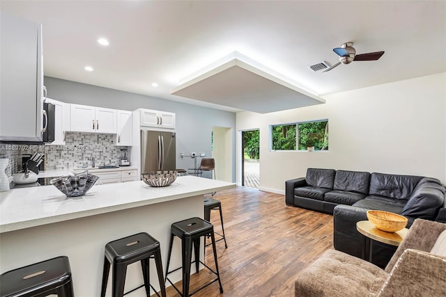 kitchen with a breakfast bar, light hardwood / wood-style flooring, decorative backsplash, appliances with stainless steel finishes, and white cabinetry