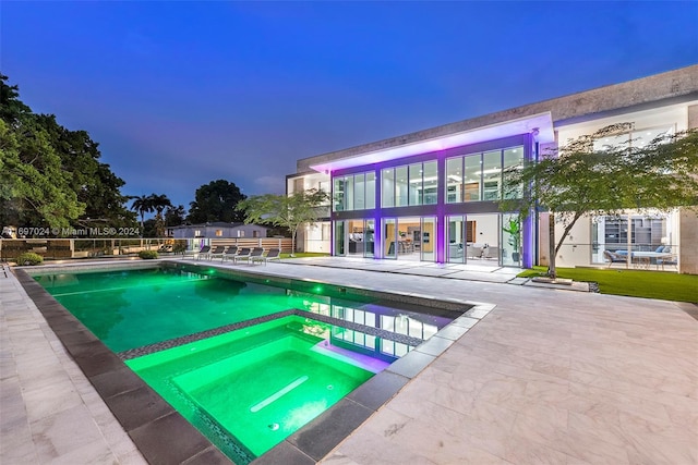 pool at dusk with an in ground hot tub and a patio