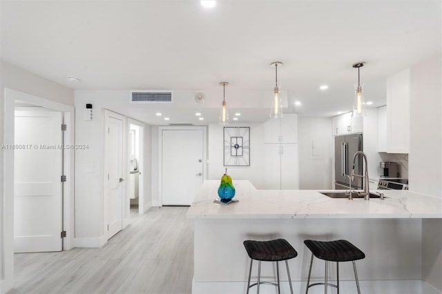 kitchen featuring high end refrigerator, white cabinets, sink, light stone counters, and kitchen peninsula