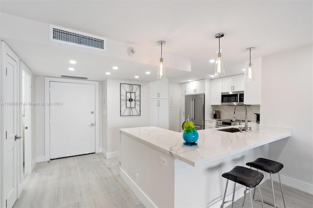 kitchen featuring hanging light fixtures, kitchen peninsula, light stone countertops, appliances with stainless steel finishes, and white cabinetry