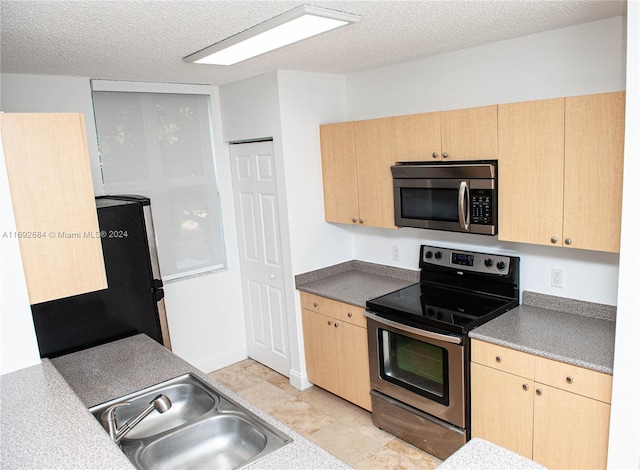 kitchen with light brown cabinets, a textured ceiling, and appliances with stainless steel finishes