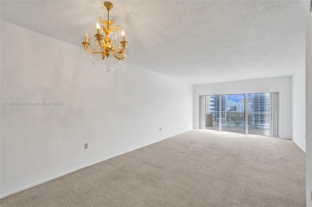 spare room featuring carpet flooring, a textured ceiling, and an inviting chandelier