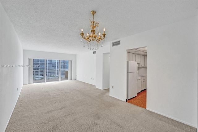 spare room featuring light carpet, a textured ceiling, and a chandelier