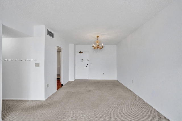 unfurnished room with light carpet, a textured ceiling, and an inviting chandelier